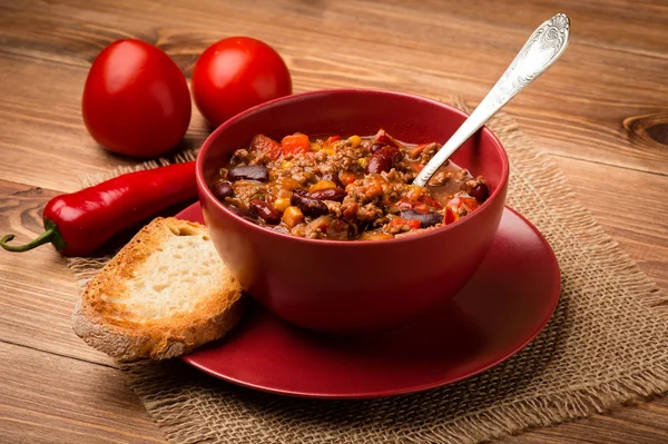 Chili con Carne serviert in der roten Schüssel auf dem hölzernen Hintergrund. — Stockfoto