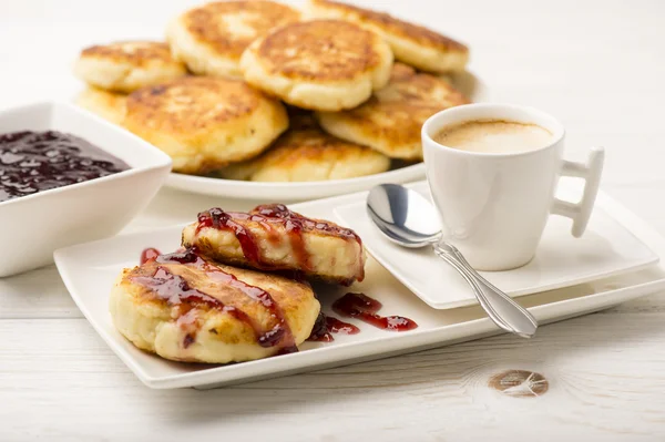 Panquecas de queijo cottage com uma xícara de café no fundo de madeira branca . — Fotografia de Stock