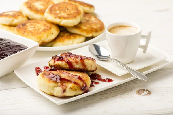 Panquecas de queijo cottage com uma xícara de café no fundo de madeira branca . — Fotografia de Stock