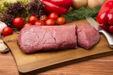 A piece of raw veal and fresh vegetables on the wooden table. clipart