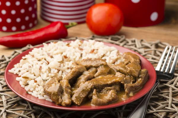 Carne estofada y arroz en el plato rojo sobre fondo de madera marrón . — Foto de Stock