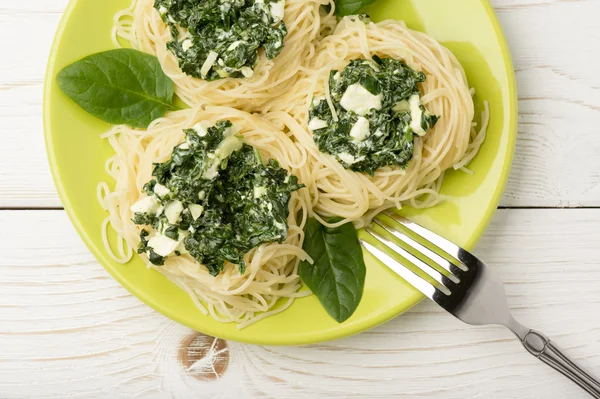 Pasta italiana con spinaci e feta su piatto verde sullo sfondo di legno . — Foto Stock