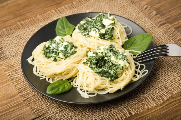 Italian pasta with spinach and feta on black plate on the wooden background. — Stock Photo, Image