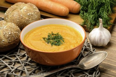 Masanın üzerine portakal kapta havuç krem çorba.