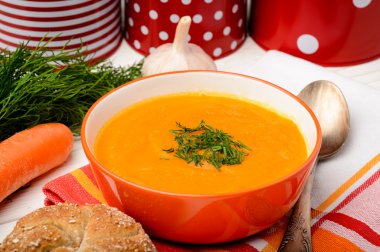 Masanın üzerine portakal kapta havuç krem çorba.