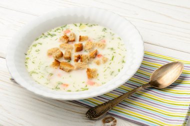 Beyaz ahşap masa üzerinde beyaz kasede peynir çorbası.