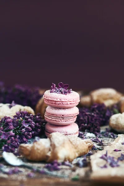 Pastry and macaroons with lilac flowers on table — Stock Photo, Image