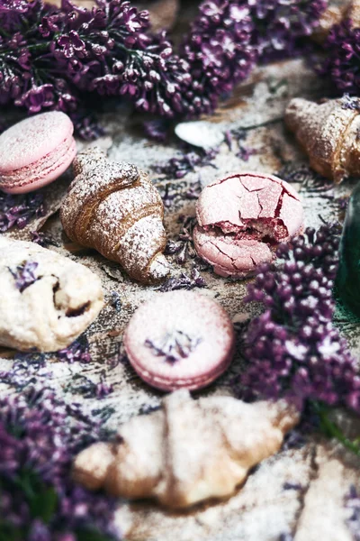 Pastry and macaroons with lilac flowers on table — Stock Photo, Image