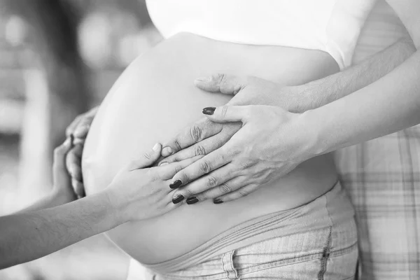 Беременная женщина с руками мужа на животе — стоковое фото