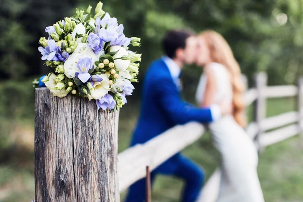 Wedding bouquet on fence with kissing couple — Stock Photo, Image