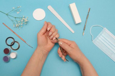 Kadın eli, renkli bir arka planda tırnak derisini söker. Tırnaklarına dikkat et. Manikür için aksesuarlar.