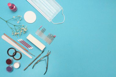Manikür, pedikür ve mavi arka planda tırnak tasarımı ekipmanlarının üst görüntüsü. Beyaz çiçekler. Metin için yer.