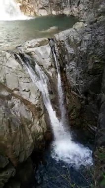 Ağaçların arasında taşlı iki şelaleden oluşan bir şelale. Dikey.