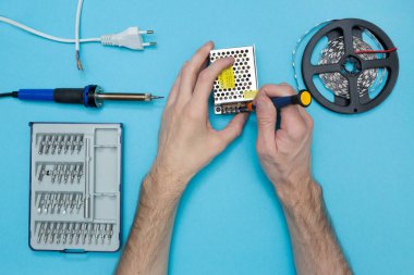 LED şeridini bir güç kaynağına bağlıyorum. Arkaplan bağlantısı araçları. Eller çerçevede..