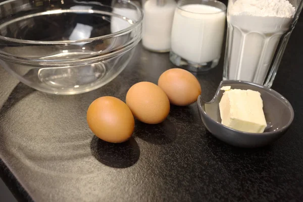 Preparação para cozinhar panquecas. Os ingredientes na mesa preta são farinha de trigo, ovos, manteiga, açúcar, sal, leite. — Fotografia de Stock