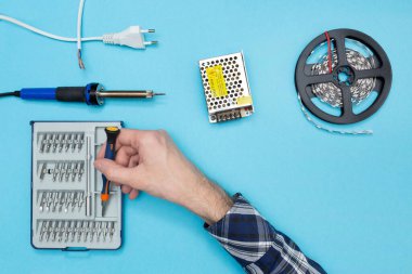 Bir LED şeridini güç kaynağına bağlamak için araçlar. Genç mühendis bir tornavida alıyor..