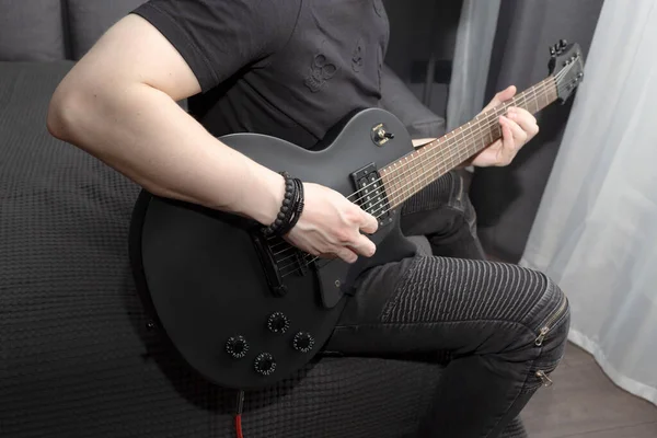 Genç bir adam evde siyah bir elektro gitar çalar. Gitar çalmayı öğreniyorum. Evde kişisel gelişim. Kazma kullanıyor..