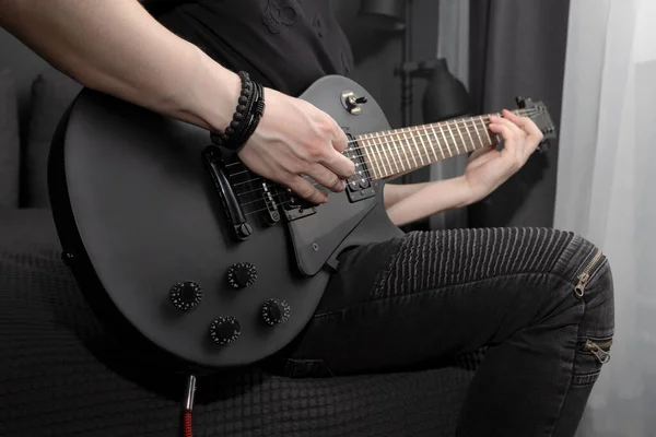 Evde siyah elektro gitar çalan genç bir adam. Gitar çalmayı öğreniyorum. Hobiler ve evde rahatlık. Kazma kullanıyor.