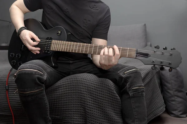 A young man playing hard rock a black electric guitar at home. Learning to play the guitar. Self-development at home. — Stock Photo, Image