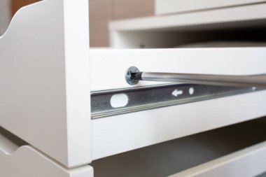 Mobilya montajı. Usta yatağın başucundaki masayı kuruyor. İşçi bir tornavida kullanıyor. Yakın plan..