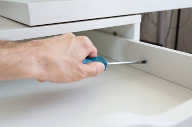 Mobilya montajı. Usta yatağın başucundaki masayı kuruyor. İşçi bir tornavida kullanıyor. Yakın plan. El ve çerçeve.