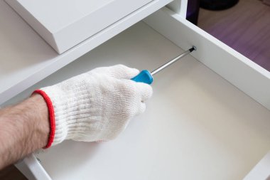 Mobilya montajı. Koruyucu eldivenlerin ustası komodinleri toplar. İşçi tornavida kullanıyor..