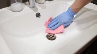 Genç adam kirli lavaboyu yıkıyor. Ellerinizi koruyucu eldivenlere koyun. Banyoyu temizliyorum. Ev temizliği konsepti. Lavaboyu siler