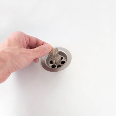 Adam banyodaki tıkanmış kanalizasyondaki kılları alıyor. Banyoyu temizliyorum. Yakın plan. Kare fotoğraf.