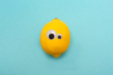 Sarı limon ve şaşı gözler. Komik bir yüz. Yuvarlak gözlü. Mavi arka plan. Tatil.