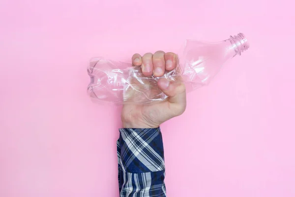 Мужчина сжимает пластиковую бутылку на розовом фоне. Против использования пластика. Переработка. Экология. — стоковое фото