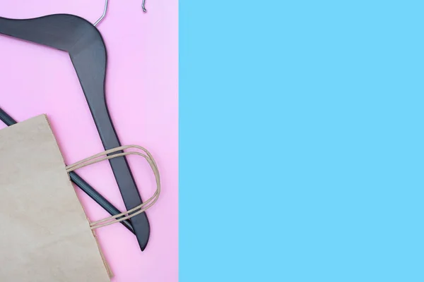 Ahşap elbise askısı pembe ve mavi arka planda. Saplı bir kese kağıdı. Uzayı kopyala Mesaj için yer. Alışveriş konsepti. Düz yatıyordu.