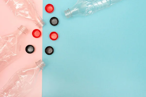 Много использованных и скомканных пластиковых бутылок на розовом и синем фоне с местом для текста. Концепция переработки. Пластиковые крышки. Раздавлена. Разумное потребление. Плоский лежал. Копирование пространства. — стоковое фото