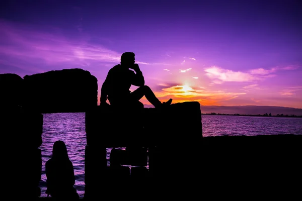 Silhueta de homem e menina sentados ao pôr do sol — Fotografia de Stock