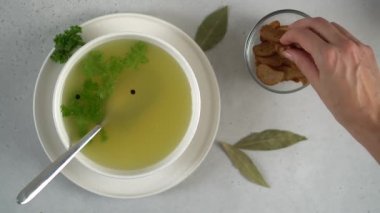 Female hand adds breadcrumbs or croutons to the bone broth.