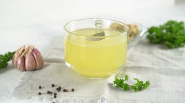 Glass mug of healthy homemade tasty turkey bone broth with garlic and bay leaf. 