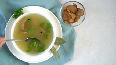 A womans hand stirs homemade chicken bone broth and takes a spoon out of a bawl
