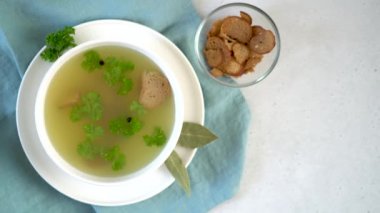 Parsley leaves, peppercorns and croutons spin in a mug of chicken bone broth.
