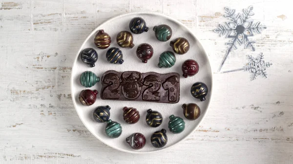 Chocolate bar 2021 with chocolate cow. Chocolate Christmas balls on white plate — Stock Photo, Image