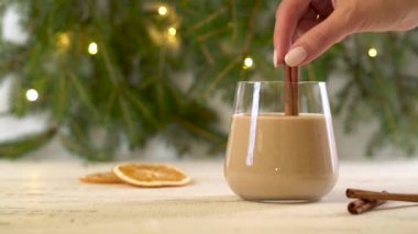 Bir kadın eli tarçın çubuğuyla ev yapımı eggnog kokteylini karıştırır..