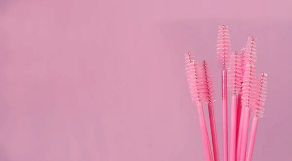Pink makeup eyebrow brushes on pink background. Eyebrow and eyelash combs. Disposable pink brush for eyelashes and eyebrows. Copy space.