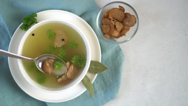 Een vrouwenhand roert kippenbotbouillon met peterselie, peperkorrels en croutons. — Stockvideo