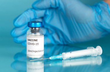 Doktorlar mavi bir tıbbi eldiven verip ampulü Covid-19 aşısıyla koruyor. Şırıngayla Coronavirus aşısı. 