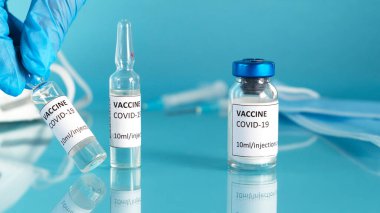 Doktorlar mavi bir tıbbi eldiven verdiler. Kovid aşısı için bir aşı şişesi aldılar. Coronavirus aşı şişesi, ampuller, şırıngalar ve mavi arka planda yüz maskesi..