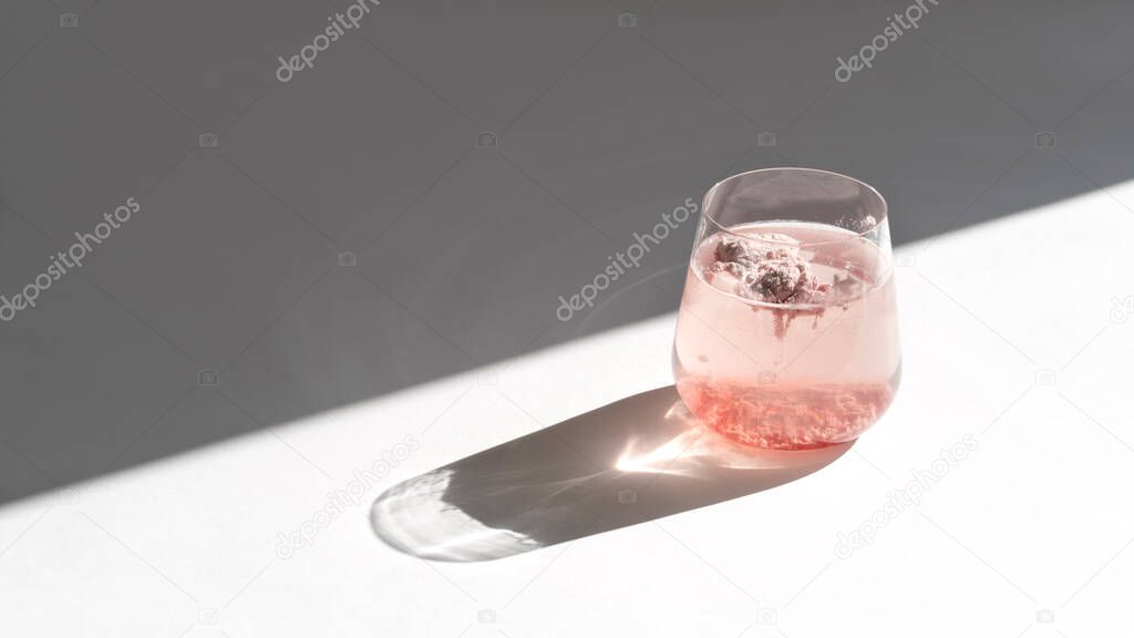 Glass of natural strawberry collagen protein powder in glass of water for skin regeneration. Trendy food additives. White background with sunlight and deep shadow of glass. Hard sunlight.