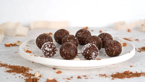 Homemade healthy raw vegetarian dessert energy balls with nuts, dates, peanut butter, cocoa powder, coconut flakes and oats on white plate with sunlight. Healthy eating. Fitness snack. Selective focus