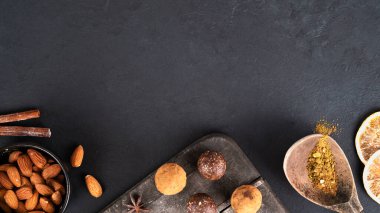 Tarçın çubuklu enerji topları, anason, portakal dilimleri ve koyu ahşap kesme tahtasında badem. Kakao tozuyla kaplı ev yapımı çiğ vejetaryen tatlısı yok. Sağlıklı beslenme. Seçici odaklanma. Boşluğu kopyala