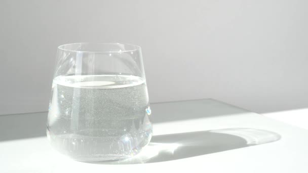 Vaso de agua pura fresca sobre fondo blanco con luz solar y sombra profunda de vidrio. Luz dura. Acercar. — Vídeo de stock