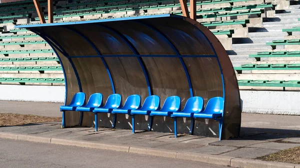 Empty blue plastic team players bench under shades in the stadium of football. Coach and reserve benches in a soccer field. Soccer bench seats.