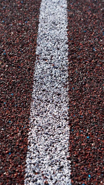 Běžet na sportovním stadionu. Červená běžecká nebo běžecká závodní guma s bílými liniemi a texturou. Prázdné pozadí běžící stopy. Selektivní zaměření. — Stock fotografie