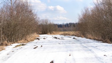 Köy yolunda eriyen karlar. Gökyüzünde bulutlarla güneşli bir gün. Bahar geliyor..